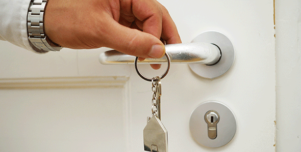 Hand an Türklinke mit Schlüsselanhänger in Form eines Hauses