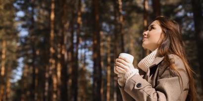 Frau mit Tasse in der Hand unter Bäumen