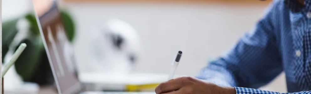 Student mit Laptop schreibt in ein Notizheft