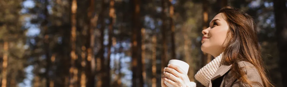 Frau mit Tasse in der Hand unter Bäumen