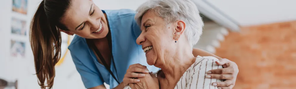 Junge, weibliche Pflegekraft lacht herzlich mit Seniorin