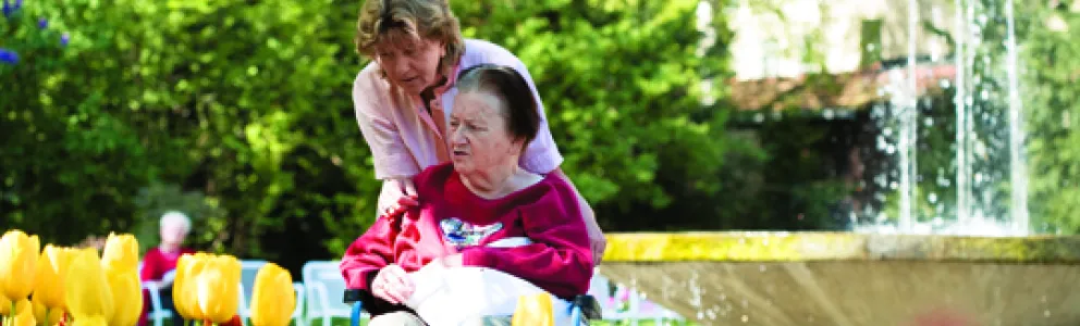 Pflegekraft schiebt Frau in Rollstuhl