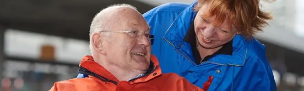 Mann wird im Rollstuhl von Ehrenamtlicher geschoben.