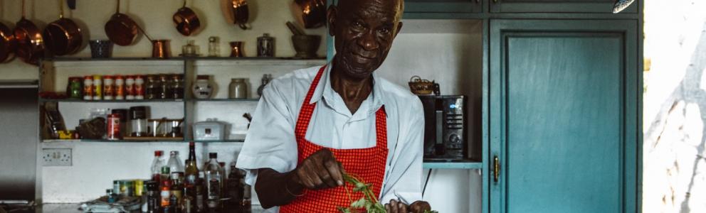 Älterer Mann steht in einer Küche und wäscht Gemüse