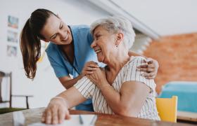 Junge, weibliche Pflegekraft lacht herzlich mit Seniorin